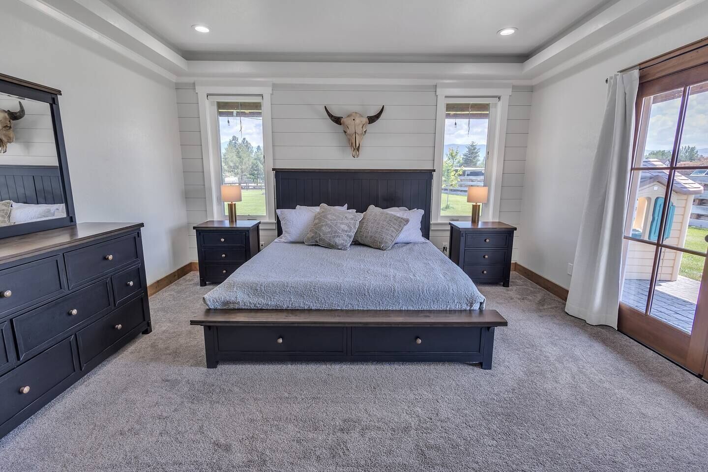 Une chambre à coucher avec un grand lit, deux tables de chevet, une commode et une décoration représentant une tête de taureau.