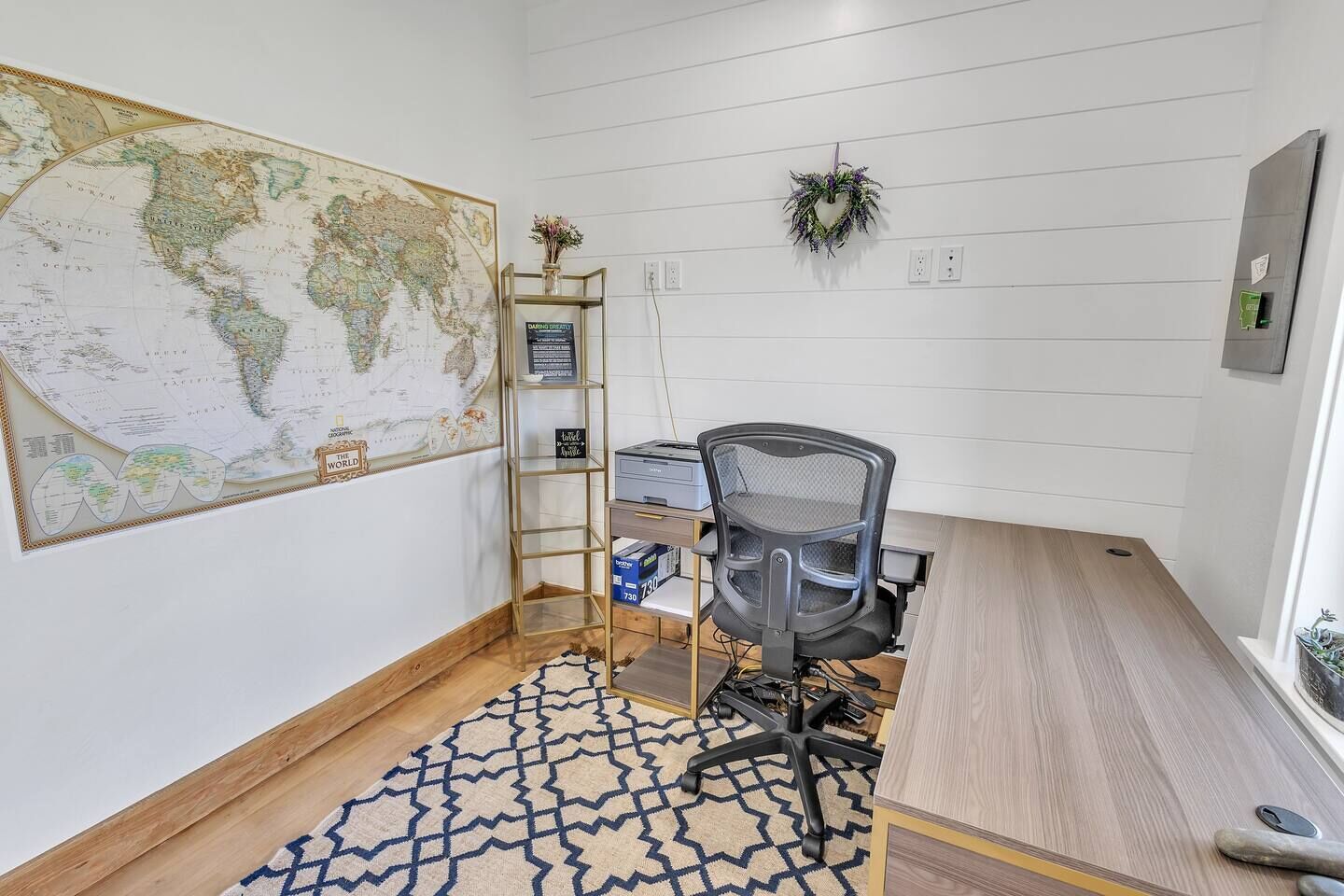 A small office with a large world map, a desk with a computer, and a chair.