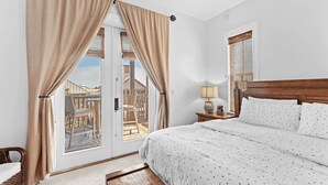 A bedroom with a large bed, a nightstand, a lamp, and a view of a balcony.