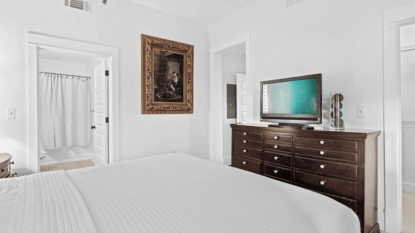 A bedroom with a large bed, a dresser, a television, and a framed picture on the wall.
