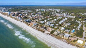 An aerial view of a coastal residential area with houses, a beach, and a distant view of the ocean.
