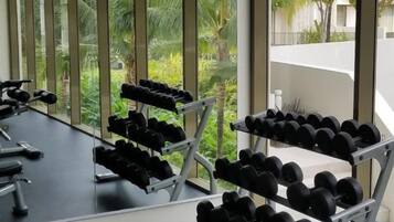 A gym with dumbbells arranged on racks, large windows, and a view of greenery outside.