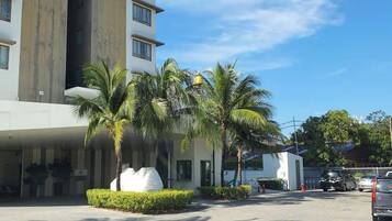 A hotel with a modern design, featuring a multi-story building, palm trees, and a parking area.