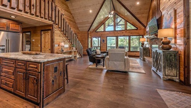 Interior espacioso de una cabaña con una amplia escalera de madera, una zona de cocina, un comedor y una sala de estar con chimenea.