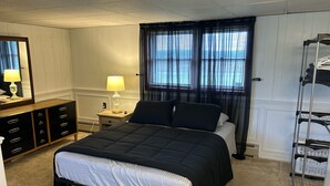 Une chambre à coucher comprenant un lit, une table de chevet avec une lampe, une commode, une fenêtre avec des rideaux et un étendoir à linge.
