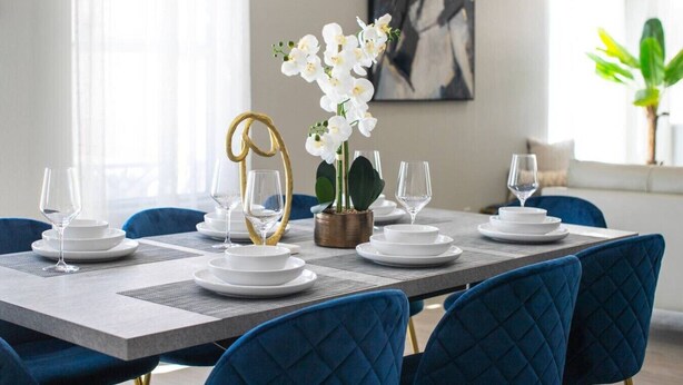 Une table à manger dressée avec de l’argenterie blanche, des verres et un centre de table composé d’orchidées blanches.