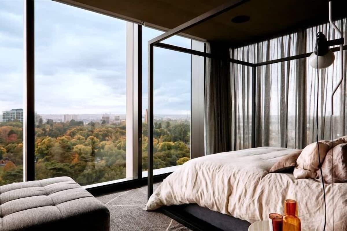 Une chambre moderne avec une grande fenêtre, un lit, un banc et une lampe.