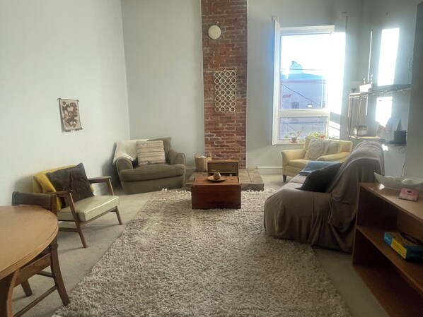 Una sala de estar con una pared de ladrillo decorativa, un ventanal grande y un rincón de descanso acogedor con una mesa de centro.