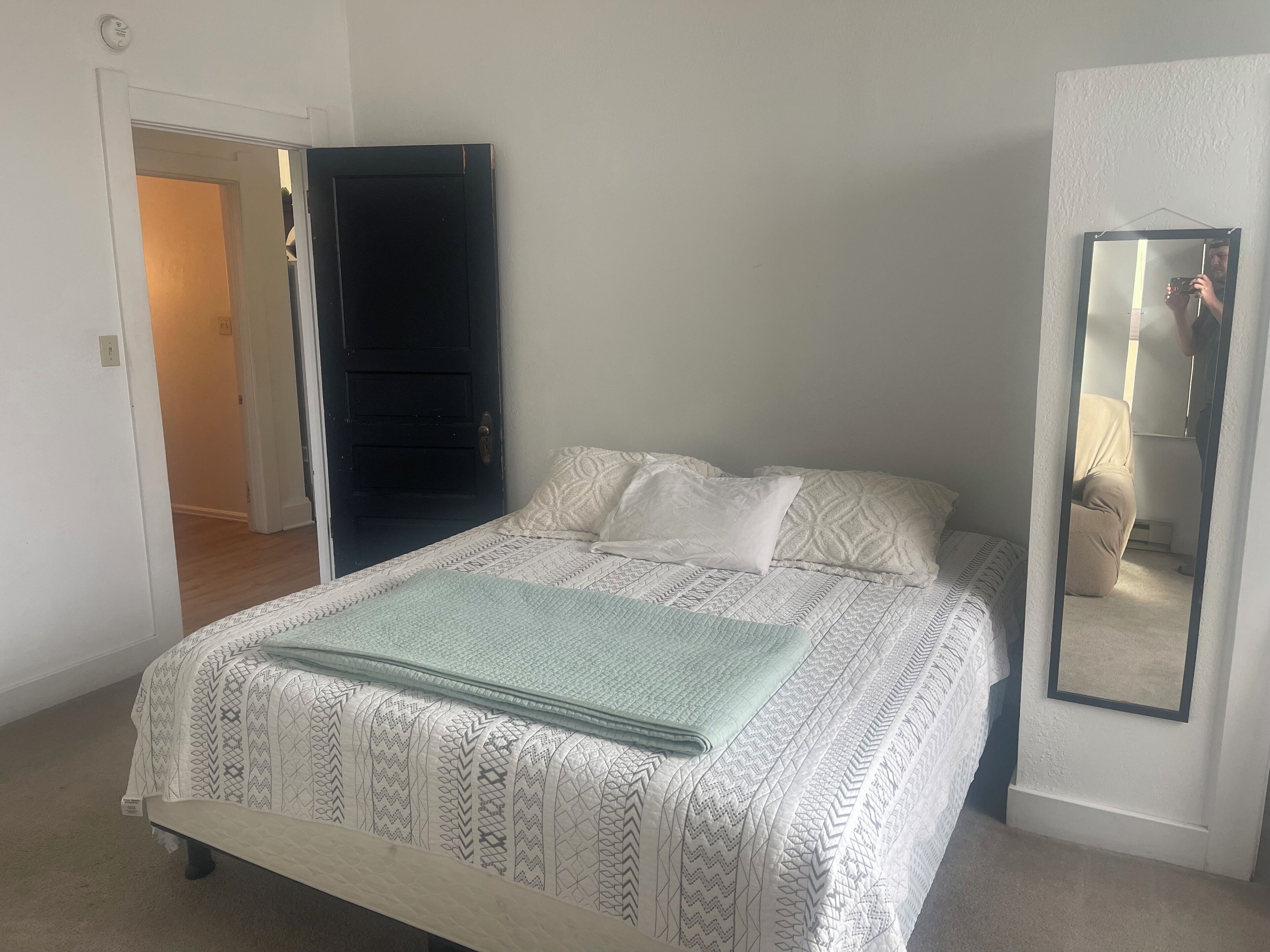 Un dormitorio con cama, espejo y puerta que da a otra habitación.