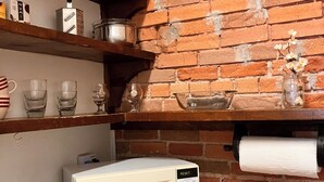 Una cocina con pared de ladrillo, microondas, tostadora y estantes con utensilios de cocina y botellas.