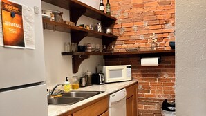 Cocina compacta con armarios de madera, lavavajillas blanco, microondas y pared de ladrillo.
