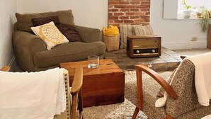 Una sala de estar acogedora con pared de ladrillo, un sofá, un sillón, una mesa de centro de madera y una radio antigua.