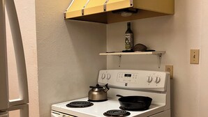 Una cocina con una estufa blanca, una campana extractora amarilla y una botella de aceite de oliva en un estante.