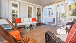Eine überdachte Veranda mit Deckenventilator, Korbmöbeln und einem weißen Sofa mit roten Kissen.