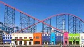 Una montaña rusa con una pista roja y una serie de edificios coloridos en primer plano.