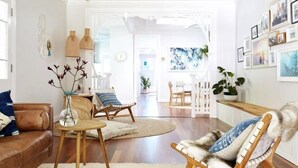 Ein modernes Wohnzimmer mit einem braunen Ledersofa, einem Holztisch und einem Stuhl mit Fellbezug. An der Wand befinden sich gerahmte Bilder und auf einem Beistelltisch steht eine Pflanze.