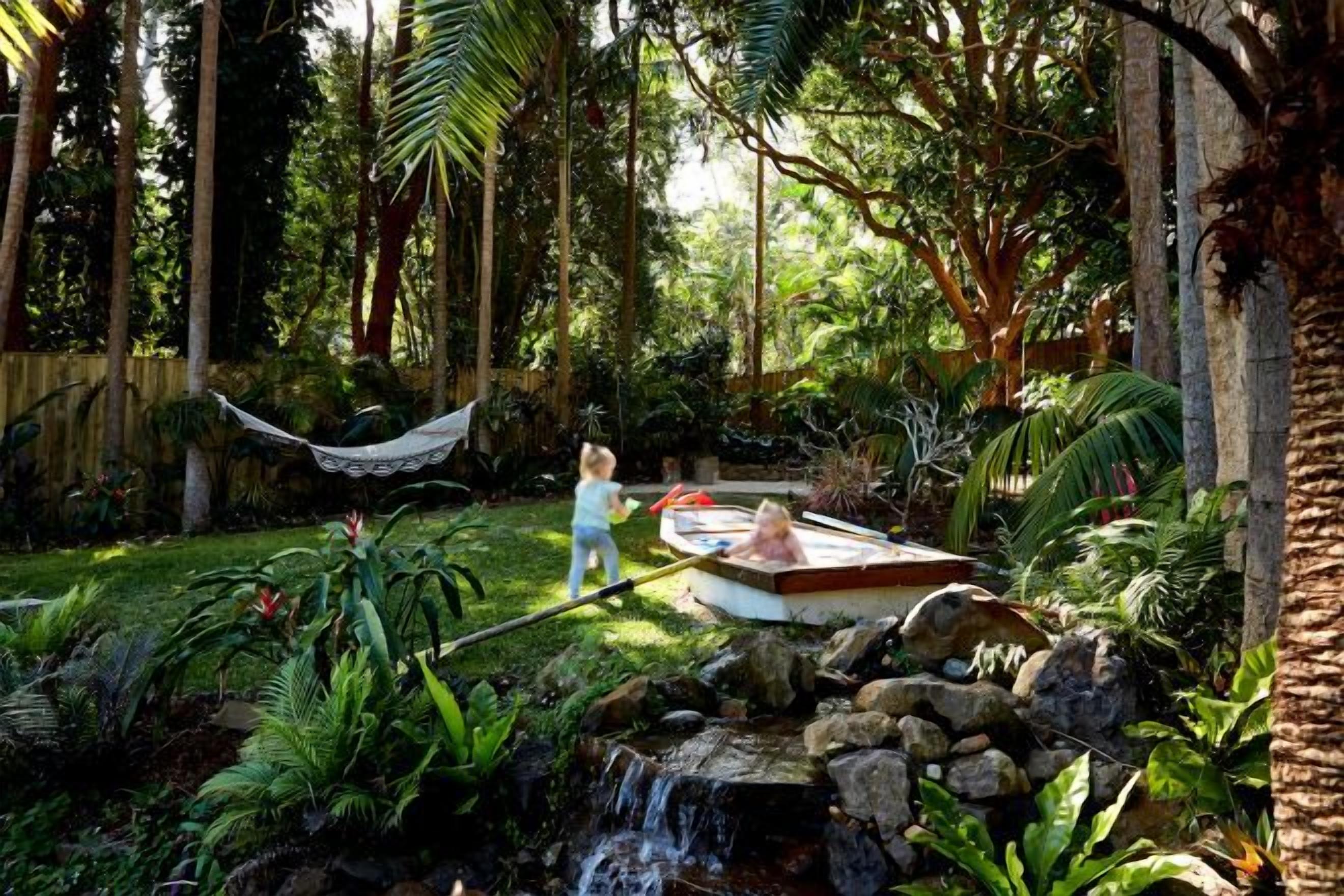 A garden with a hot tub, a hammock, and a small waterfall.