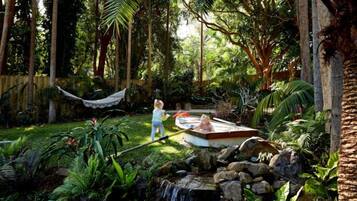 A garden with a hot tub, a hammock, and a small waterfall.