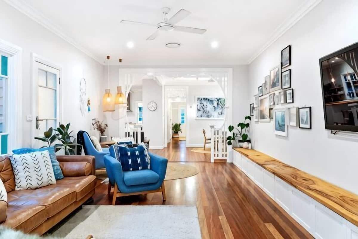 A modern living room with a brown leather sofa, a blue armchair, a wooden coffee table, and a white ceiling fan.