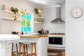Ett modernt kök med vita skåp, en köksö med barstolar, en inbyggd ugn och en hängande lampa.