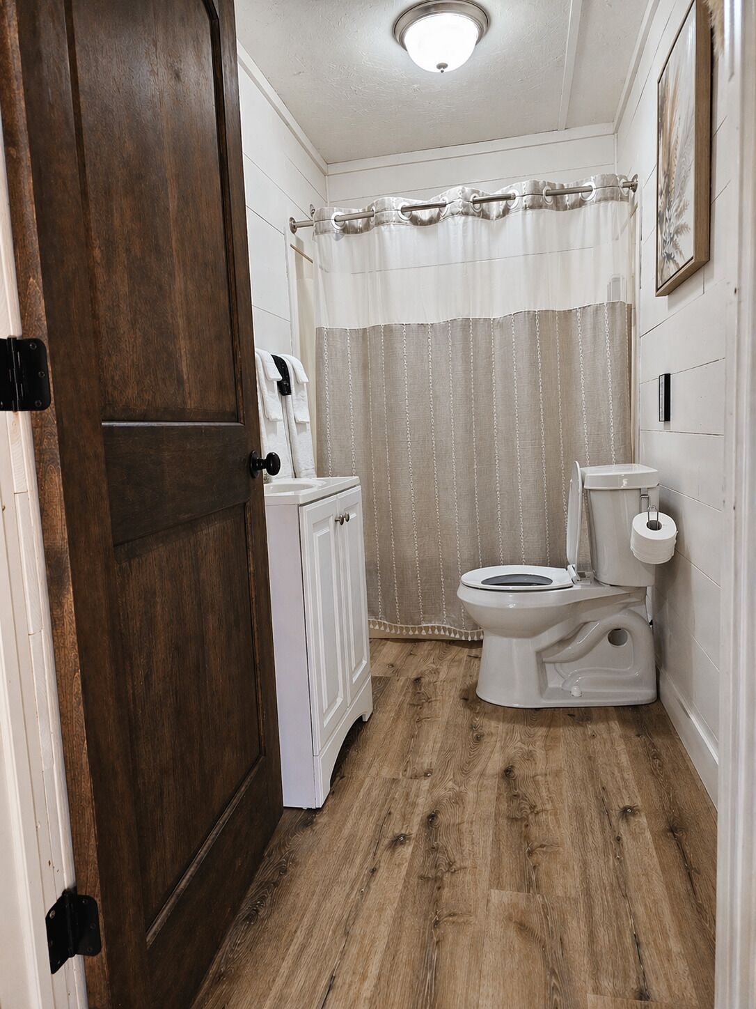 A bathroom with a wooden floor, a toilet, a cabinet, and a shower curtain.
