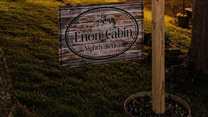 A wooden signboard with 'Enon Cabin Nightly Rental' text, a number '29' sign, and a string of lights in a grassy area at night. - Secluded • Table Rock Lake Cabin • Near Branson (Green Forest)
