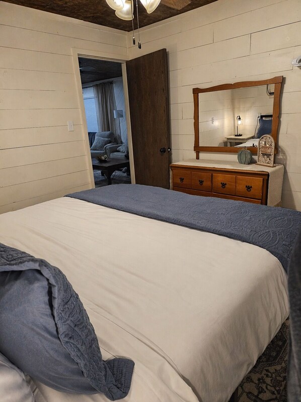 A bedroom with a bed, a dresser, a mirror, and a door leading to another room.