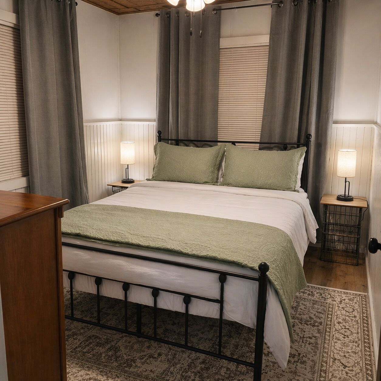 A neatly arranged bedroom with a metal bed frame, a bedside table with a lamp, and a patterned rug on the floor.