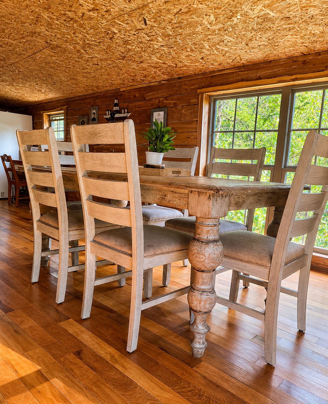 A dining area with wooden chairs and a table, large windows, and a ceiling made of wooden slats.