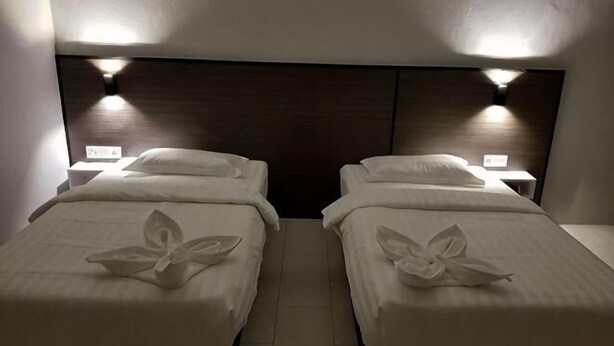 Two twin beds with white linens and a dark headboard, each with a bedside table and lamp. - Luna Guesthouse (Semporna)