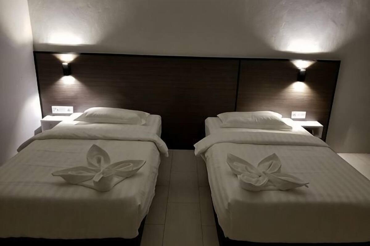 Two twin beds with white linens and a dark headboard, each with a bedside table and lamp.