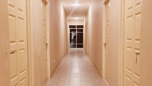 A corridor with doors on both sides, leading to a room with a glass door at the end. - Luna Guesthouse (Semporna)
