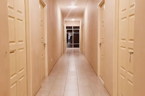A corridor with doors on both sides, leading to a room with a glass door at the end. - Luna Guesthouse (Semporna)