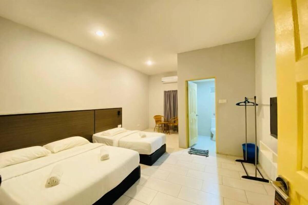 A hotel room with two beds, a chair, a coat rack, and a bathroom visible through an open door.