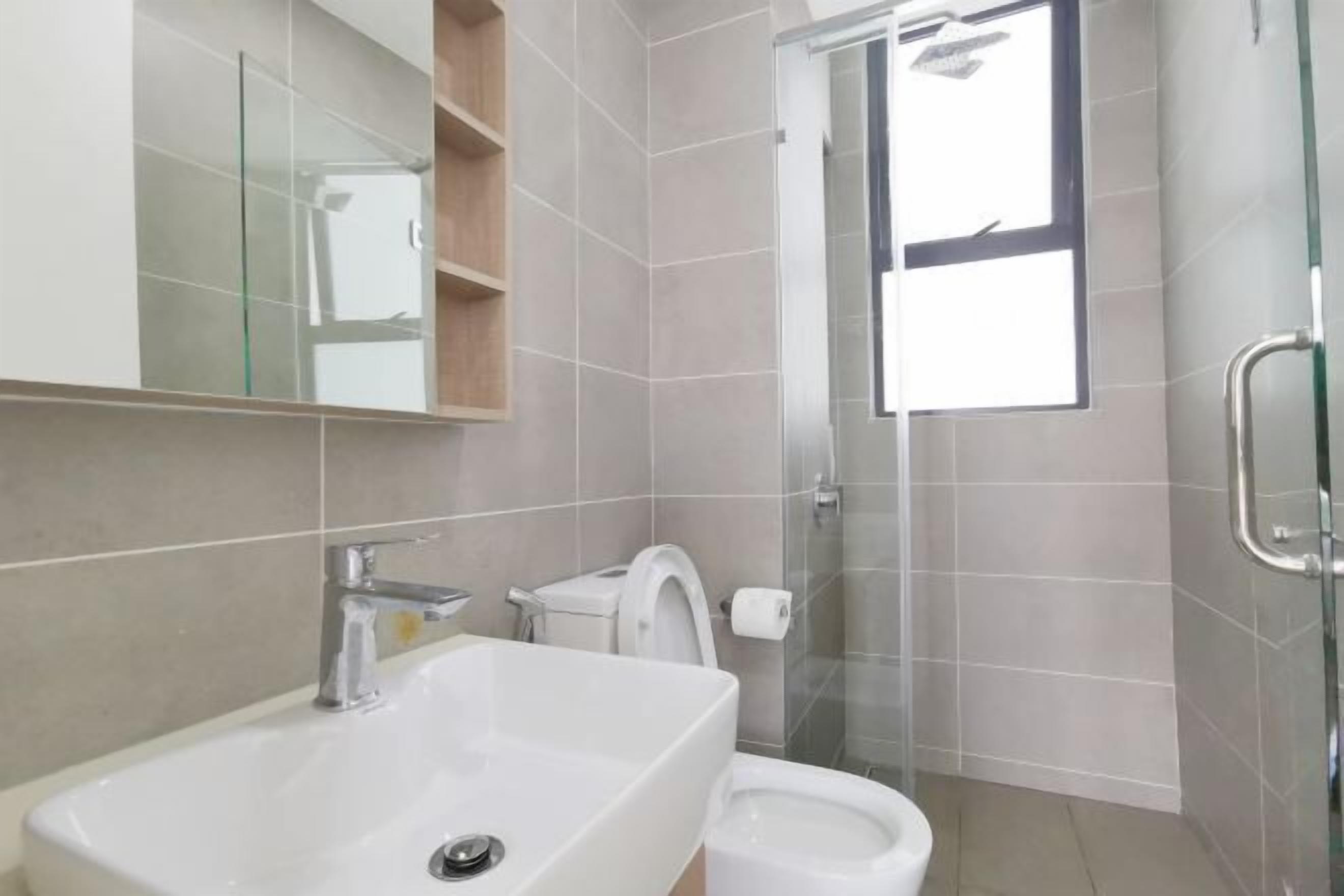 A modern bathroom with a large sink, toilet, and bidet. There is a glass shower enclosure and a window providing natural light.