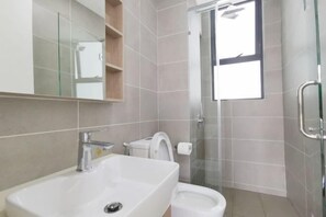 Ein modernes Badezimmer mit einem großen Waschbecken, Toilette und Bidet. Eine Duschkabine aus Glas und ein Fenster sorgen für natürliches Licht.