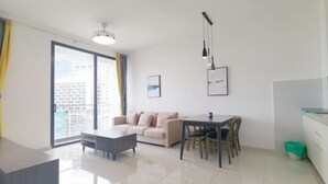 Una sala moderna con sofá, mesa de centro, mesa de comedor y sillas. Se aprecia un ventanal con cortinas, una lámpara de techo e imagen enmarcada en la pared.