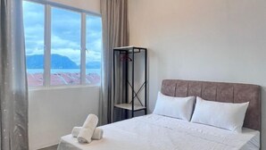 Ein Hotelzimmer mit Bett, Fenster mit Bergblick, einer hängenden Garderobe und einem Handtuch auf dem Bett.
