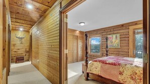 A log cabin bedroom with a bed, a wooden wall, a window, and a door.