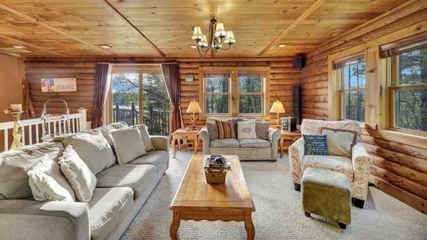A log cabin interior with a sofa, armchairs, a coffee table, and a chandelier.
