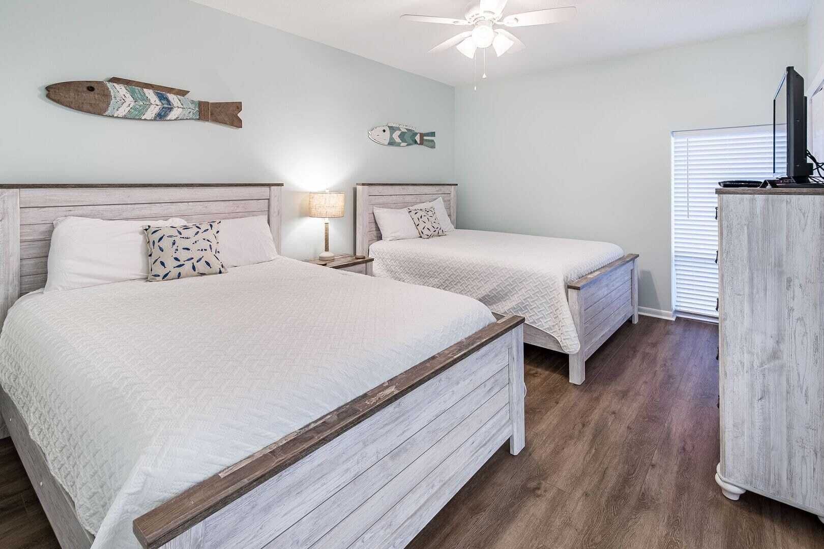 Quarto com duas camas, cabeceira de madeira, ventilador de teto e decoração de peixe na parede.