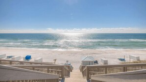 A beach view with a wooden walkway leading to the ocean, featuring beach chairs and umbrellas.