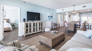 A spacious living room with a large flat-screen TV, a wicker coffee table, and a sofa.