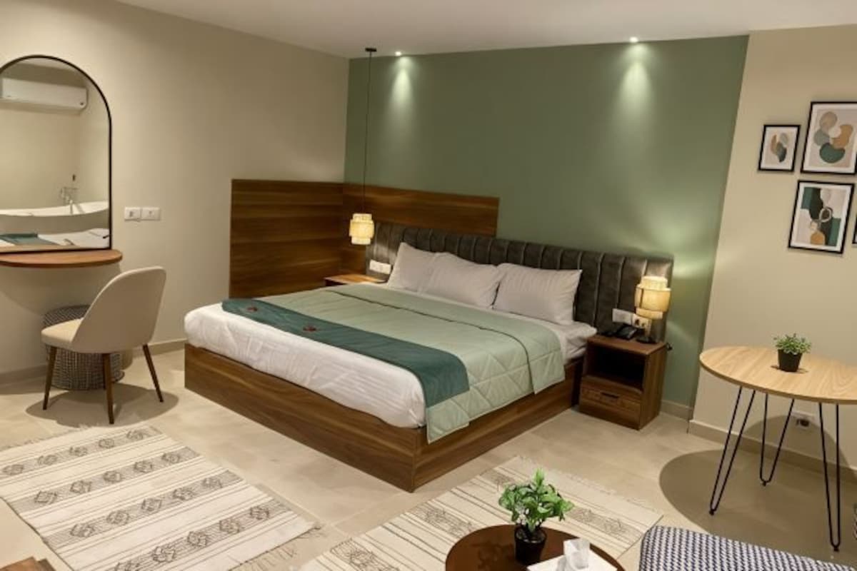 Une chambre à coucher comprenant un lit, des tables de chevet, une chaise, une petite table et un miroir.
