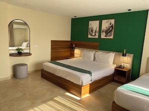 A hotel room with a large bed, a bedside table with a lamp, a small round ottoman, a mirror, and two framed pictures on the wall. - Luma Pyramids Boutique Hotel (Giza)