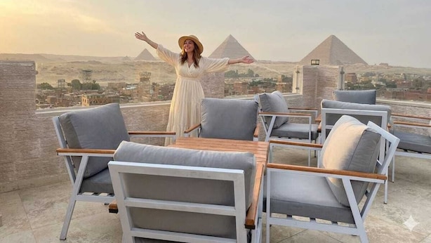 A person standing on a rooftop terrace with a view of pyramids in the background. - The Nomad Pyramids Boutique Hotel (Giza)