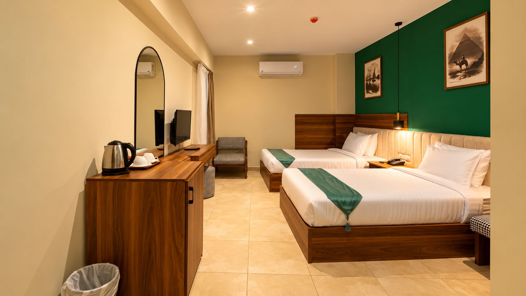 A hotel room with two beds, a wooden desk, a mirror, a television, and a trash bin.