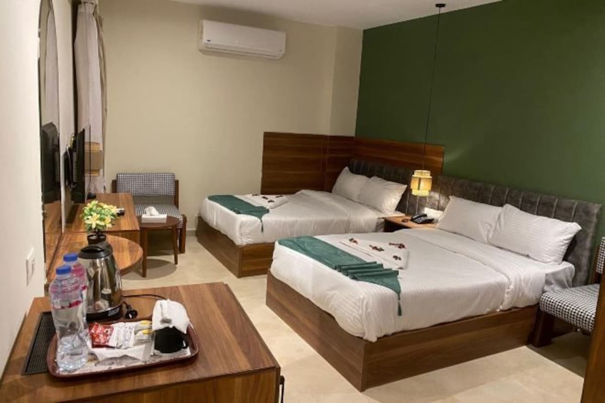 Une chambre d’hôtel avec deux lits, un bureau avec une chaise, une petite table avec une lampe et un appareil de climatisation fixé au mur.