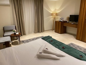 Una habitación de hotel con una cama, una silla, un escritorio, un televisor y una lámpara.