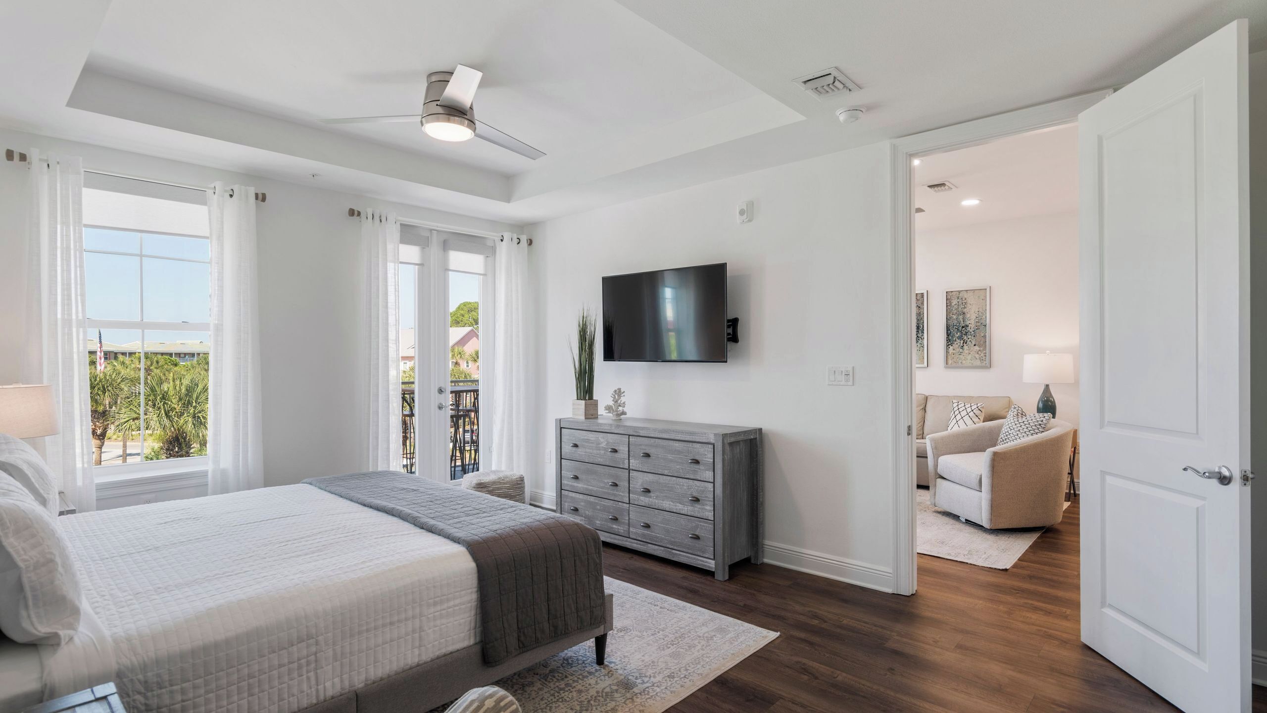 A bedroom with a bed, a dresser, a TV, and a balcony with curtains.